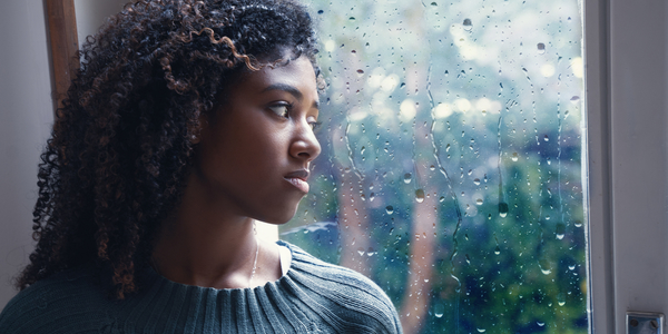 Een jonge vrouw denkt na over eenzaamheid terwijl ze naar buiten kijkt.