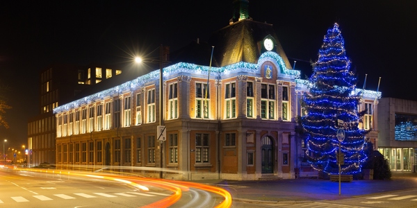 Een nachtelijk beeld van het uitgelichte districtshuis van Wilrijk met kerstboom voor de gevel.