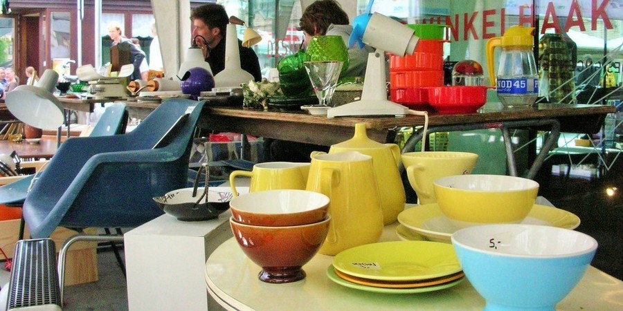 Een paar mensen kijken tussen de design- en tweedehandsartikelen op een overdekte markt. Een paar mensen kijken tussen de design- en tweedehandsartikelen op een overdekte markt.