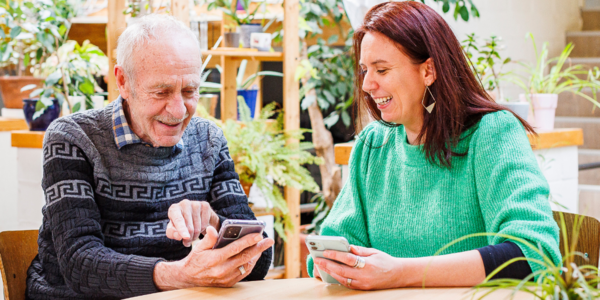 Een vrouw en een oudere man kijken lachend naar hun smartphone