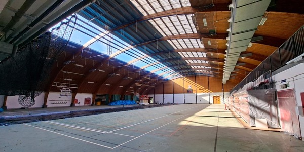 De eerste lichtstraat is uit het dak verwijderd en het zonlicht valt op de oude sportvloer en de ingeklapte tribunes.