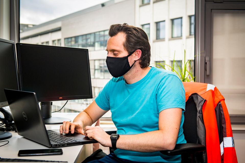 Man typt op een laptop en draagt een mondmasker.