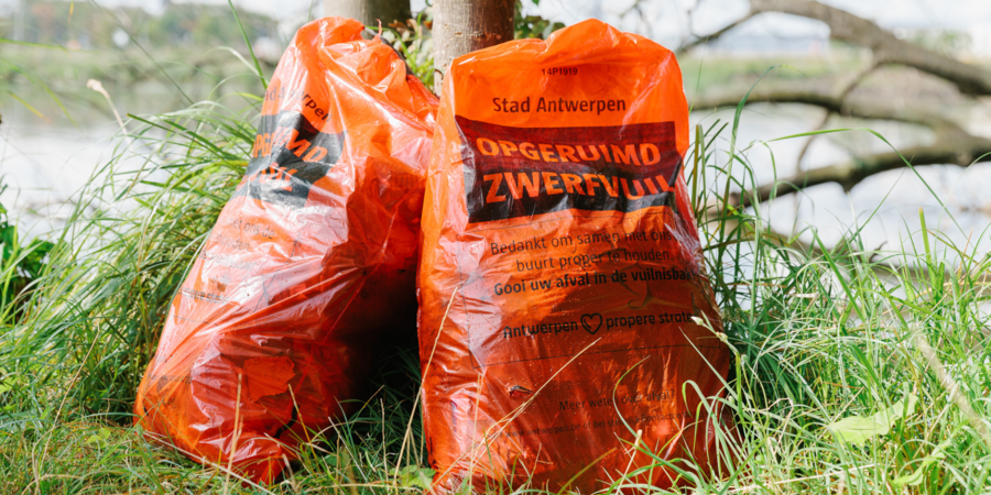 Twee rode zwerfvuilzakken staan tegen een boom. Twee rode zwerfvuilzakken staan tegen een boom.