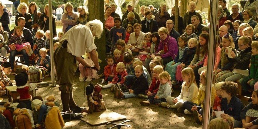 Man heeft poppen aan touwtjes vast, kinderen kijken naar het schouwspel Man heeft poppen aan touwtjes vast, kinderen kijken naar het schouwspel