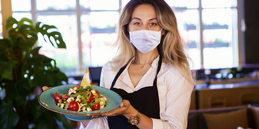 Een vrouw met een mondmasker serveert een bord met een lekkere salade. Een vrouw met een mondmasker serveert een bord met een lekkere salade.