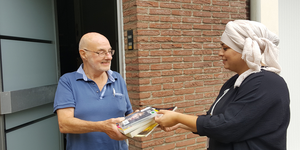 Een vrouw geeft boeken aan een man die in zijn voordeur staat.