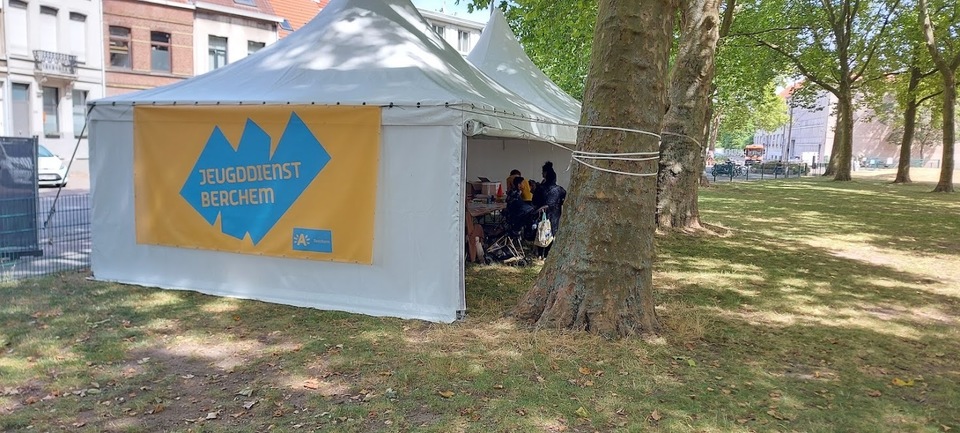 een tent met een banner van jeugddienst Berchem op het De villegaspark.