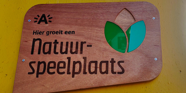 houtenbord met de tekst: hier groeit een natuurspeelplaats