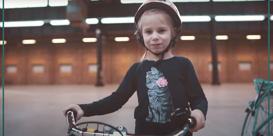 Meisje met fietshelm op dat naast haar fiets staat met de handen aan het stuur