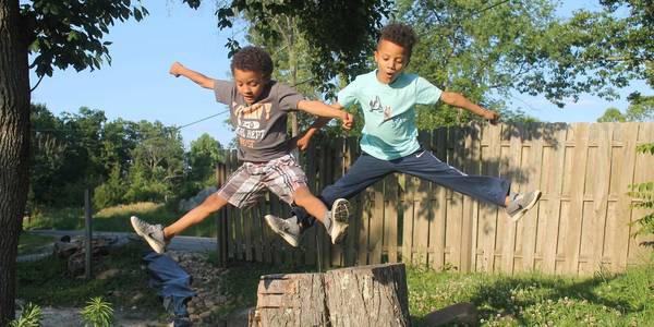 2 jongens springen over een boomstronk.