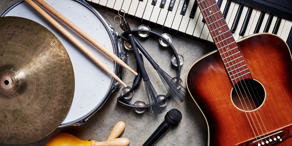 Een verzameling muziekinstrumenten waaronder gitaar, drums, een piano en een microfoon.