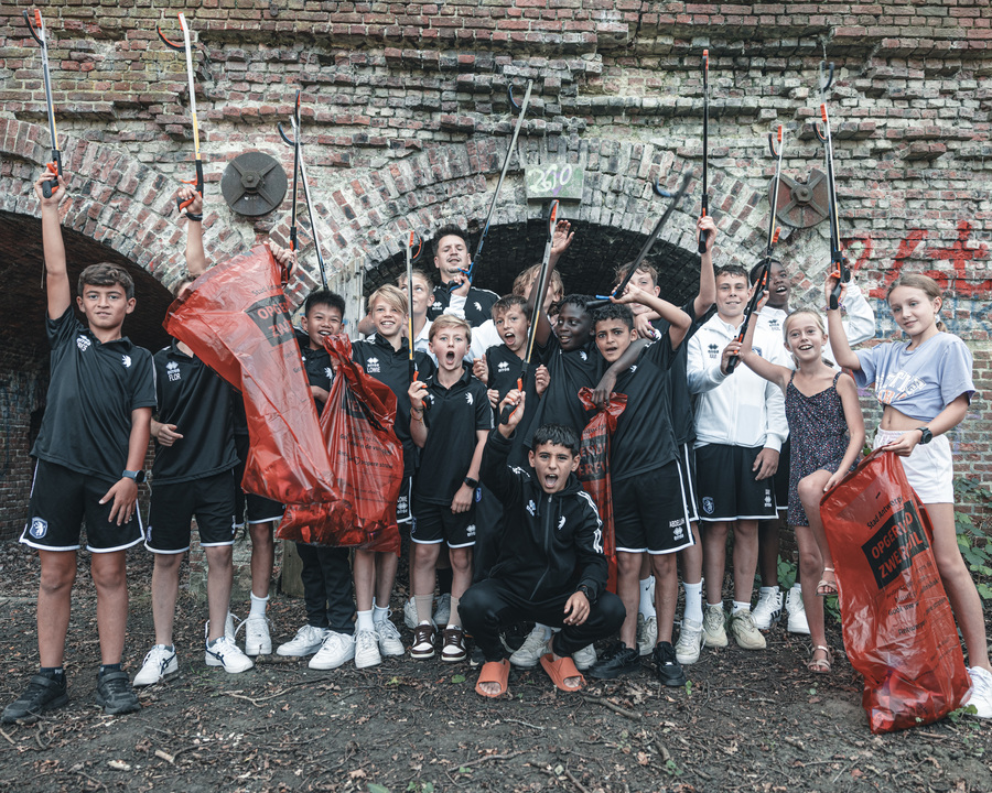 Groepsfoto van jeugdspelers van voetbalclub Beerschot met rode vuilniszakken.