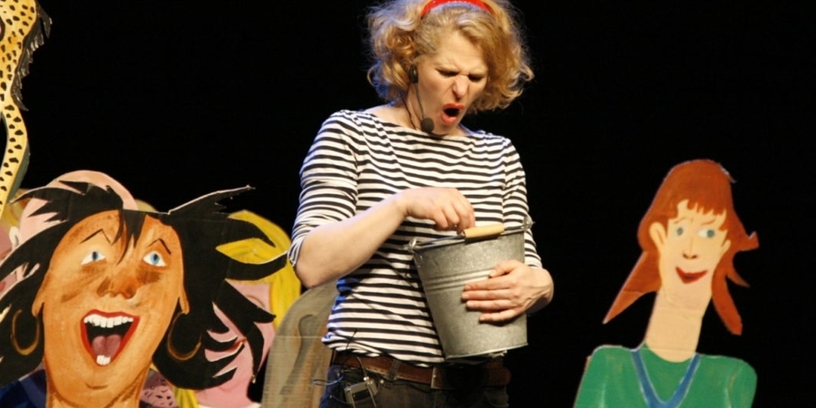 Een vrouw staat op een podium en houdt een emmer vast. Naast haar enkele bordkartonnen figuren. Een vrouw staat op een podium en houdt een emmer vast. Naast haar enkele bordkartonnen figuren.