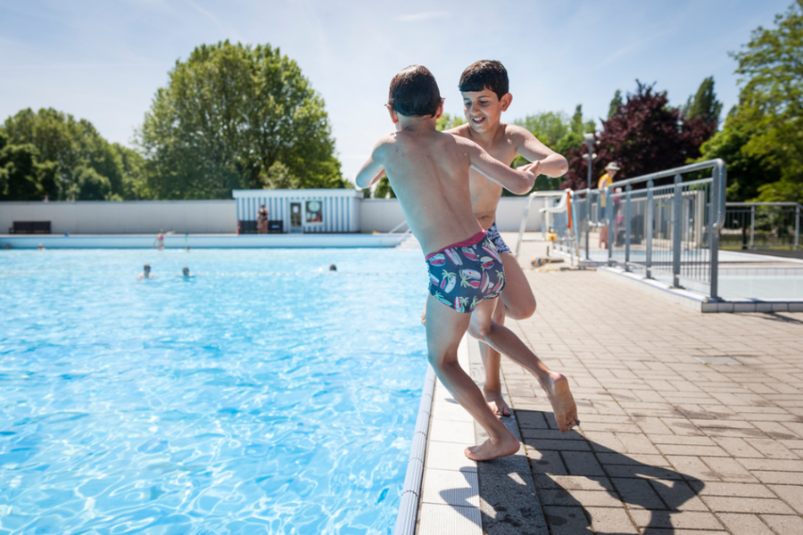2 jongens springen in het openluchtzwembad vanop de kant