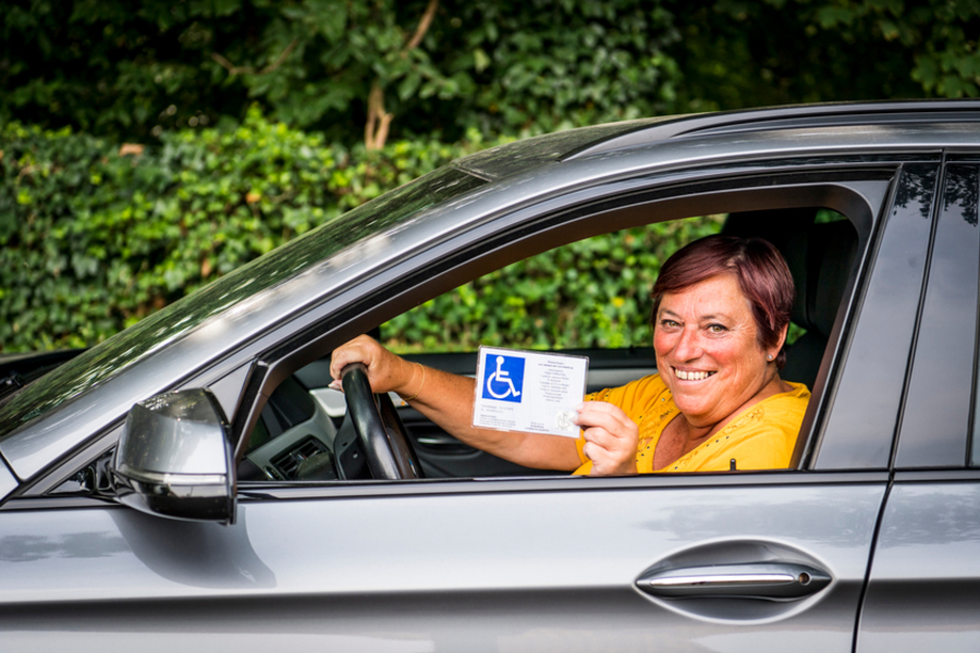 Vrouw toont haar parkeerkaart voor personen met een handicap vanuit de auto.