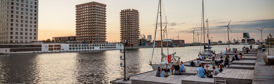 een beeld van het Kattendijkdok met aangemeerde riviercruiseshepen, het Cadixponton waarop mensen zitten en 2 zeiljachten die aan het ponton zijn aangemeerd een beeld van het Kattendijkdok met aangemeerde riviercruiseshepen, het Cadixponton waarop mensen zitten en 2 zeiljachten die aan het ponton zijn aangemeerd