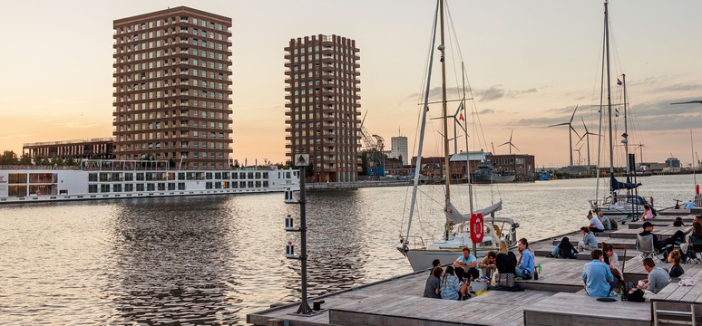 een beeld van het Kattendijkdok met aangemeerde riviercruiseshepen, het Cadixponton waarop mensen zitten en 2 zeiljachten die aan het ponton zijn aangemeerd