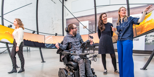 groep personen bezoekt een museum, één persoon zit in een rolstoel