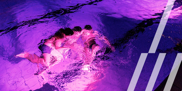 Groepje kinderen zwemt in een paars verlicht zwembad tijdens het Halloweenzwemmen