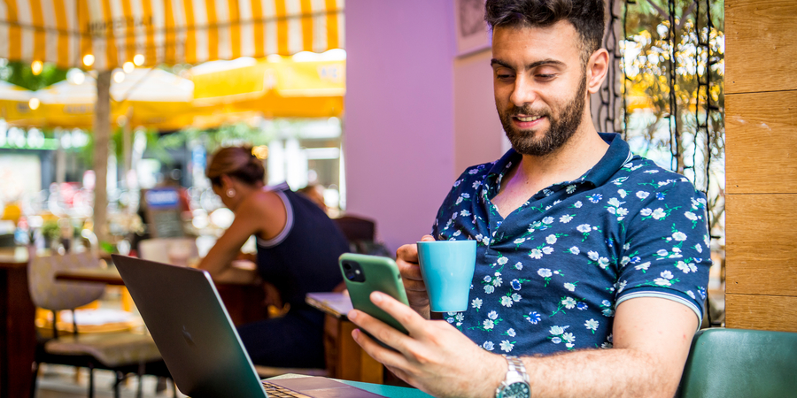 Man op terrasje met laptop en smartphone.