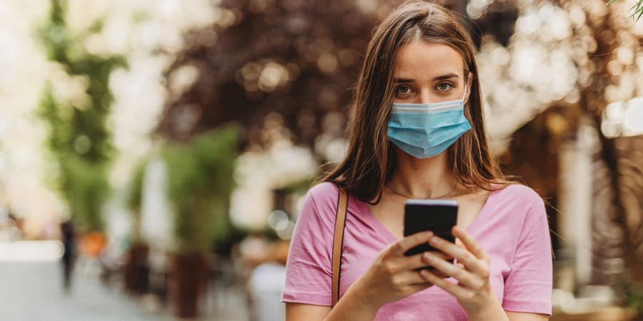 Vrouw met mondmasker die haar gsm vasthoudt Vrouw met mondmasker die haar gsm vasthoudt