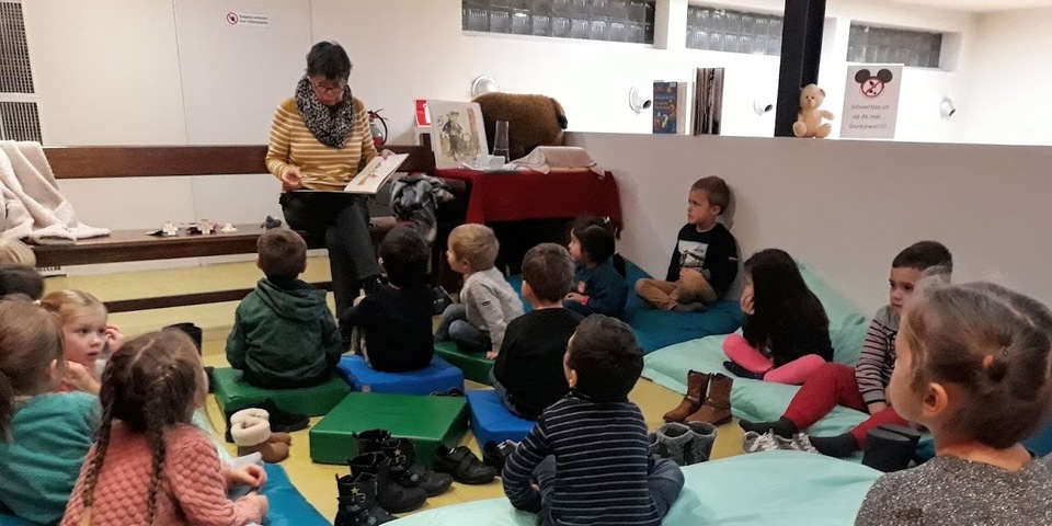 Voorlezer en luisterende kinderen tijdens een leeslekker voorleesuurtje