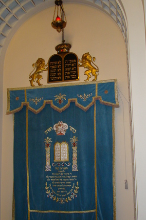 Achter het versierde doek (Parochet) bevindt zich de Ark met de Thorarollen. Het eeuwig brandend licht, de Ner Tamid hangt erboven.