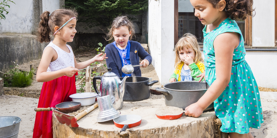 Meisjes spelen met potten en pannen in een zandbak met boomstamtafels Meisjes spelen met potten en pannen in een zandbak met boomstamtafels