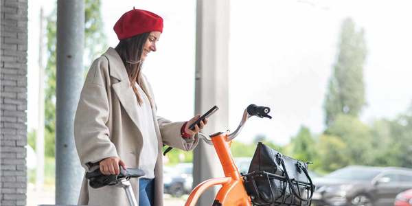 Een vrouw staat op straat met een fiets van Donkey Republic en een smartphone.