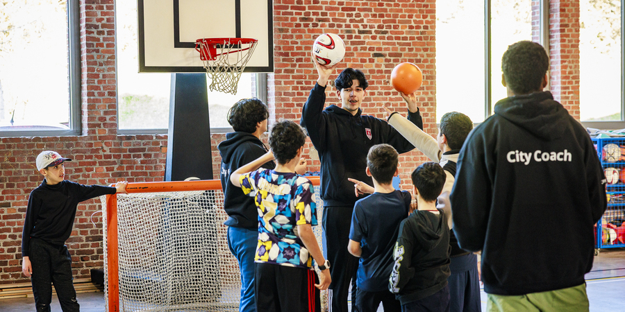 Kinderen spelen basketbal onder begeleiding van een city coach.
