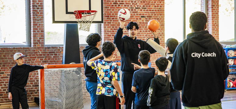 Kinderen spelen basketbal onder begeleiding van een city coach.