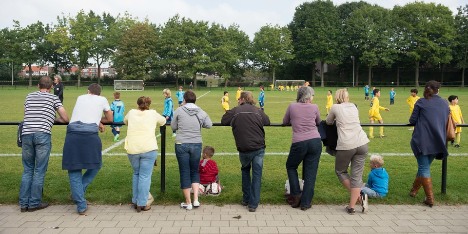 Ouders kijken naar voetbalmatch kinderen