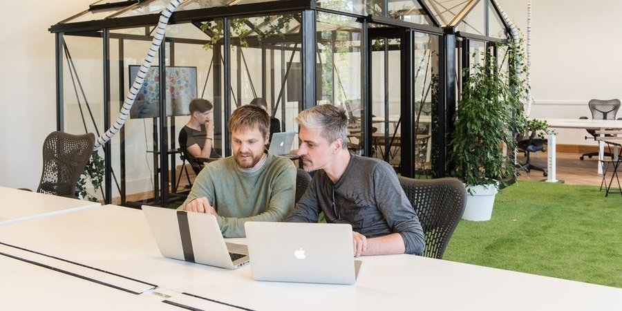 Twee mannen werken op een laptop aan een tafel in een groene kantoorruimte. Twee mannen werken op een laptop aan een tafel in een groene kantoorruimte.