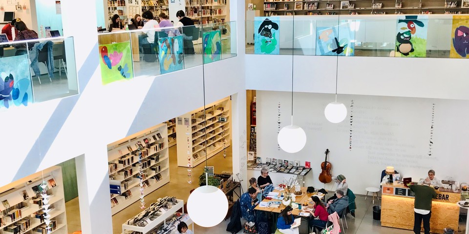 Een panoramisch sfeerbeeld van Bibliotheek Bist met bezoekers op het gelijkvloers en de eerste verdieping.