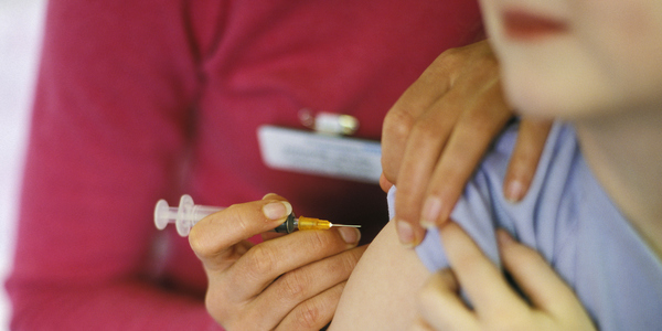 Een arts geeft een vaccin tegen mazelen aan een kind. Een vaccin tegen mazelen zit in het basisvaccinatieschema voor kinderen.