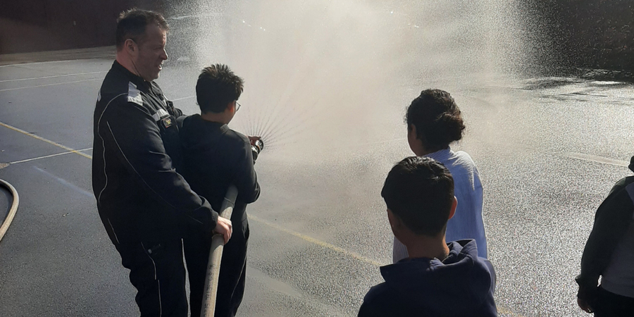 Brandweerman Tom houdt leerling tegen die spuit met brandweerslang Brandweerman Tom houdt leerling tegen die spuit met brandweerslang