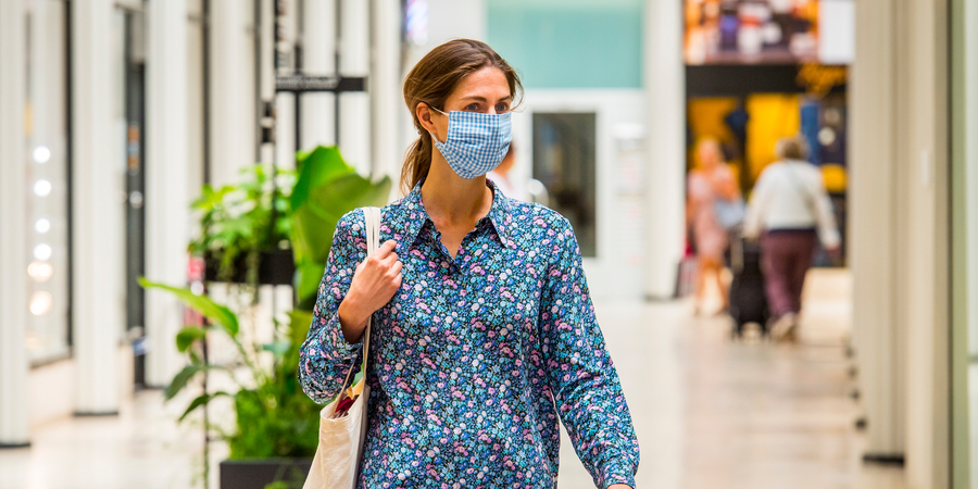 Vrouw met een mondmasker en schoudertas is aan het winkelen. Vrouw met een mondmasker en schoudertas is aan het winkelen.