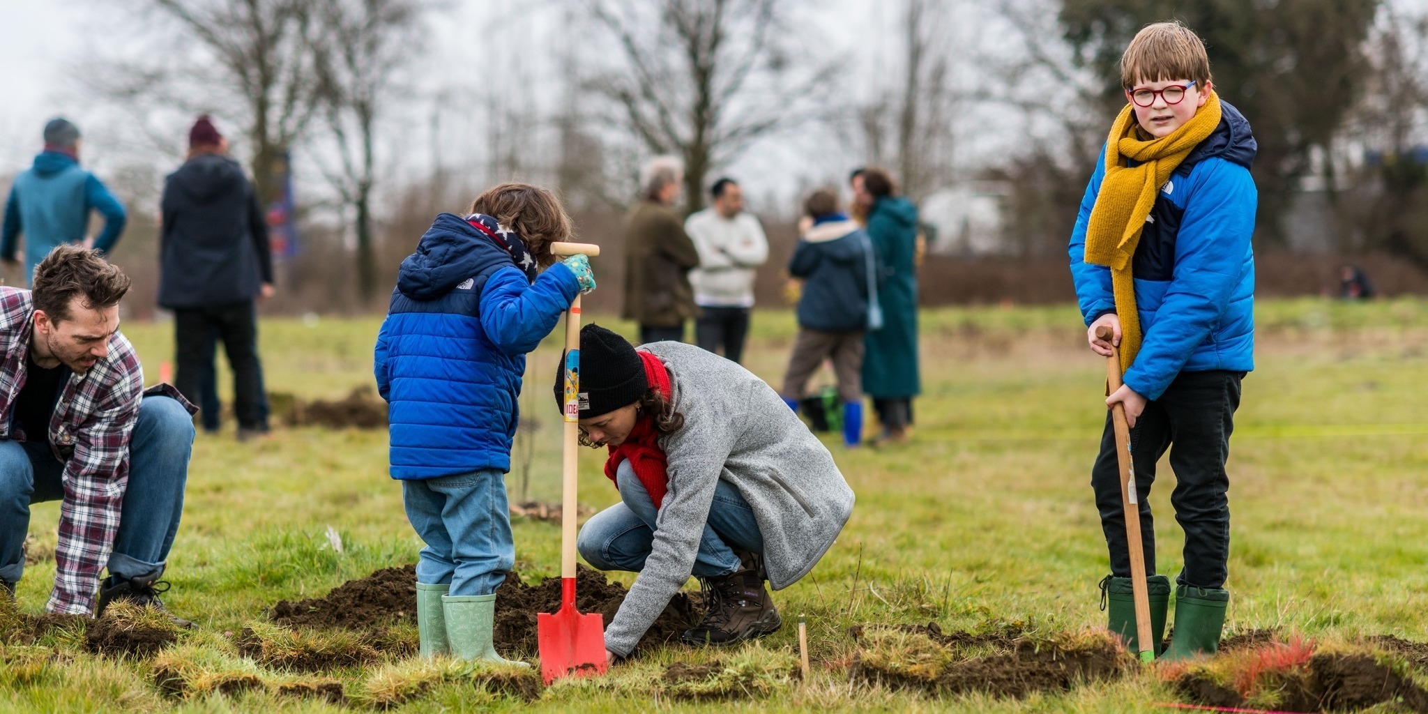 Een vrouw en twee kinderen planten een boom.