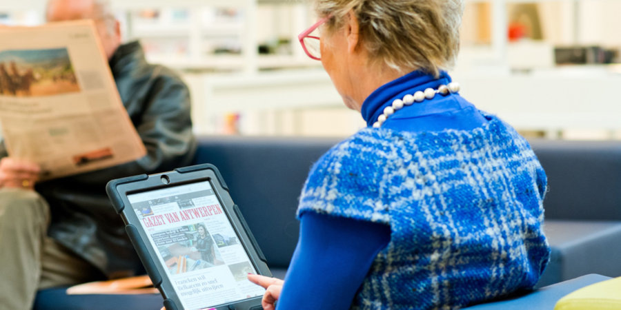 Een oudere dame leest de krant op een tablet.
