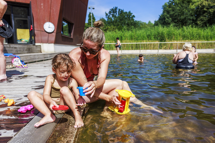 Vrouw met kind dat aan het spelen is met waterspeelgoed in het ondiepe kinderbad