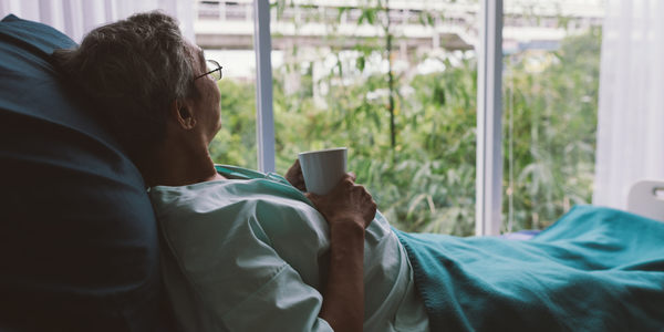 Een ziek persoon voelt zich eenzaam en kijkt vanuit een ziekenhuisbed naar buiten.