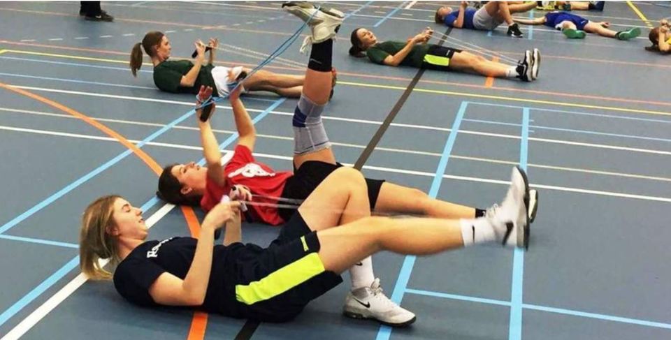 Dames liggen op een sportvloer en doen oefeningen met een touw aan de voet