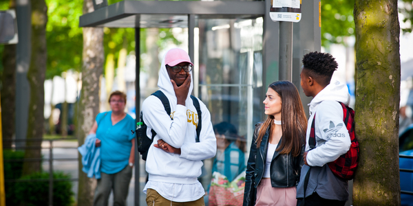 3 jongeren staan aan een bushalte te praten