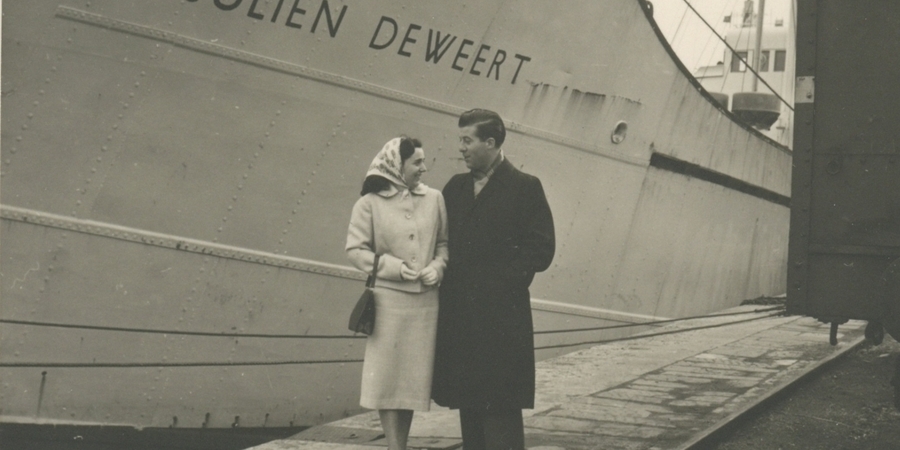 Zwartwitfoto van een koppel dat op de kaaien wandelt. Op de achtergrond een schip.