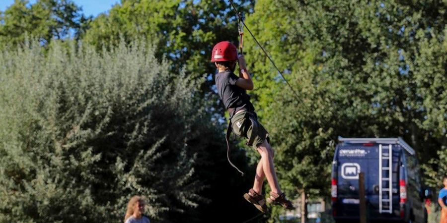 Een kind met helm hangt aan een zipline.