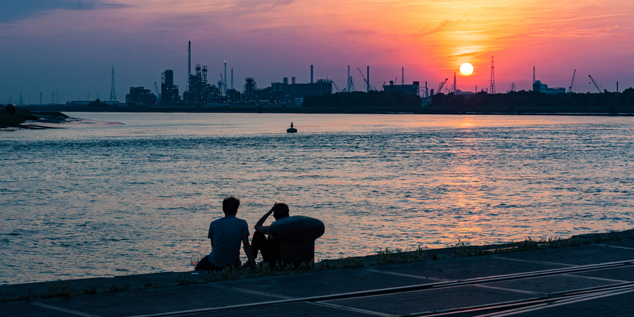 Twee mensen zitten op de Scheldekaaien en kijken bij zonsondergang naar de haven. Twee mensen zitten op de Scheldekaaien en kijken bij zonsondergang naar de haven.