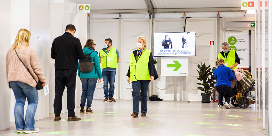 Verschillende mensen schuiven aan in het vaccinatiedorp. Stewards met een geel fluohesje helpen hen verder. Verschillende mensen schuiven aan in het vaccinatiedorp. Stewards met een geel fluohesje helpen hen verder.
