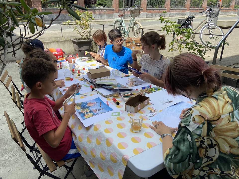 Kinderen knutselen met schaar en papier aan een lange tafel op een terras