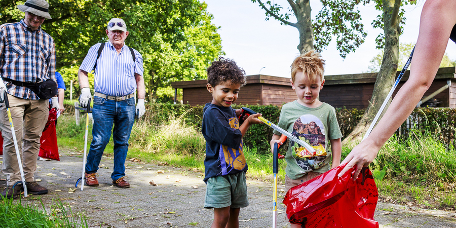 Kinderen gooien met een grijper zwerfvuil in een rode vuilniszak tijdens World Cleanup Day