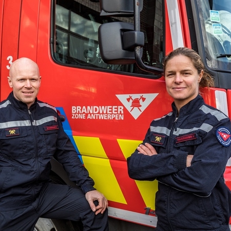 De twee brandweerlieden voor een autopomp van Brandweer Zone Antwerpen De twee brandweerlieden voor een autopomp van Brandweer Zone Antwerpen